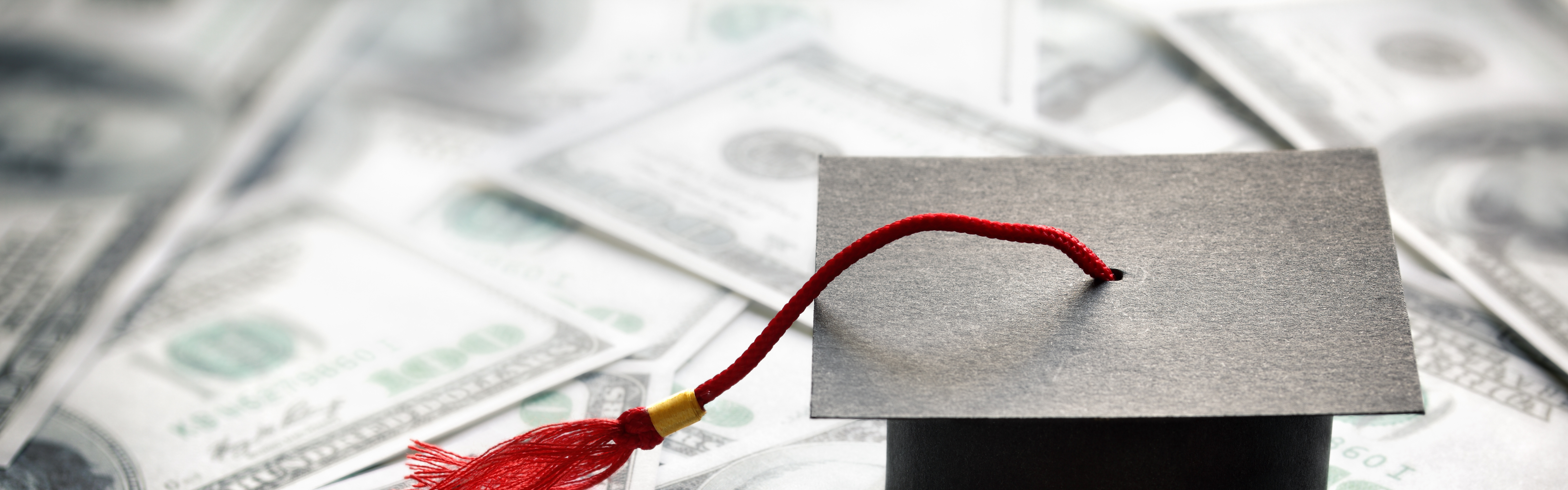 Graduation mortar board cap on one hundred dollar bills concept for the cost of a college and university education
