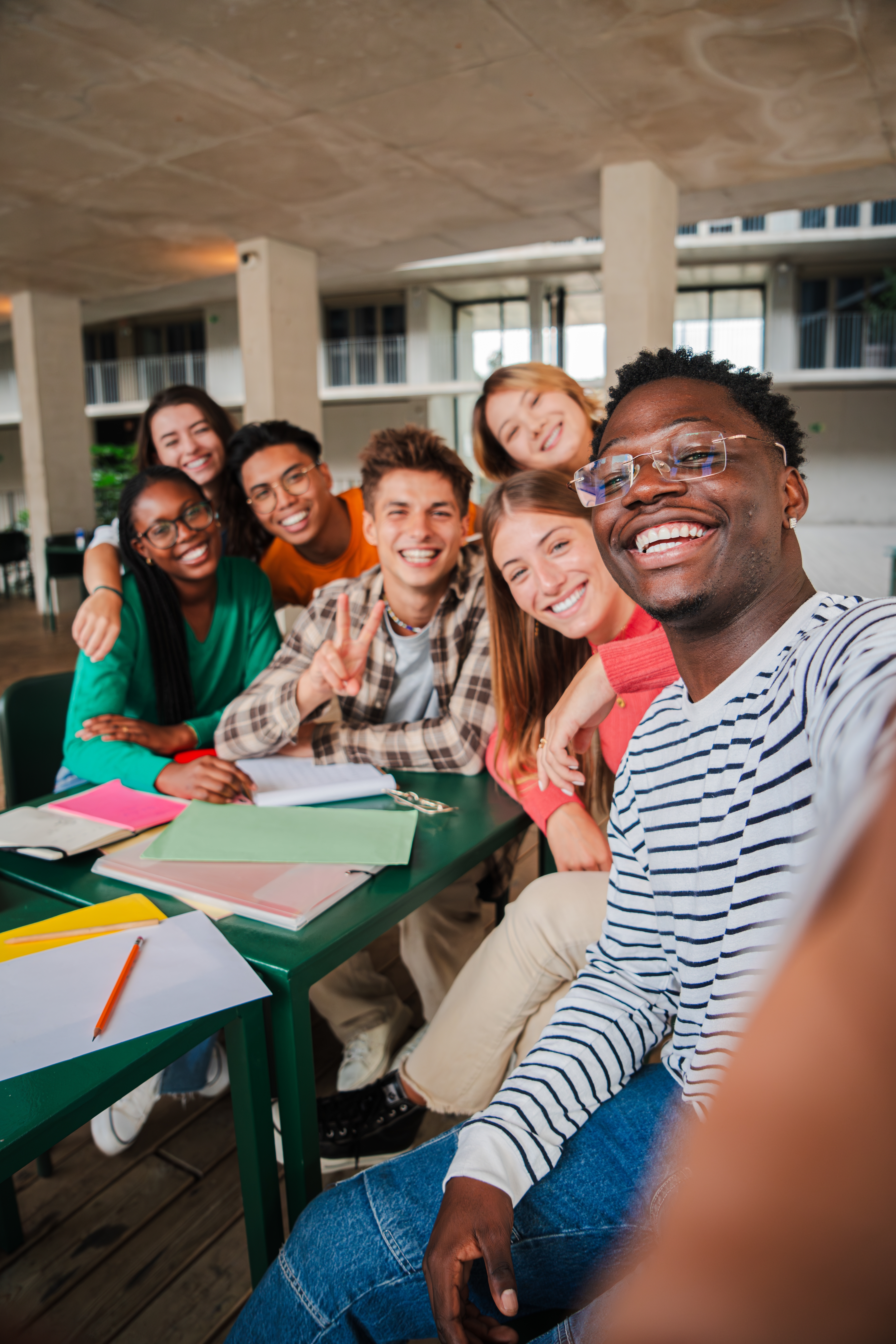Happy young students taking a vertical selfie portrait together at university library. African american guy shooting a photo with his smiley classmates on a high school meeting. Friends at academy